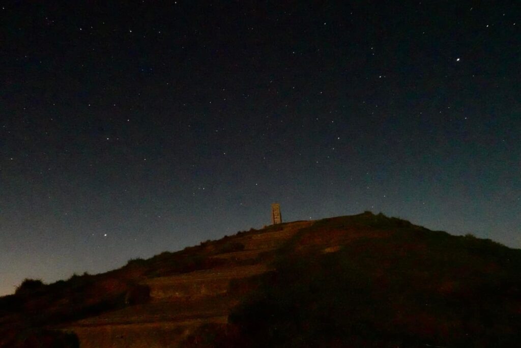 Glastonbury Tor at night under a starry sky, seen from the path below.
