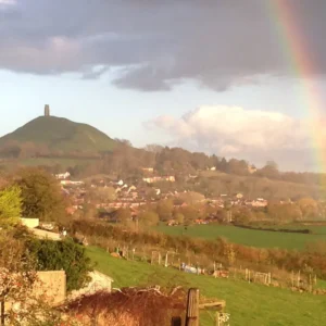 Glastonbury Tor and rainbow above the town, symbolizing a Glastonbury pilgrimage and the spiritual energy of Avalon.